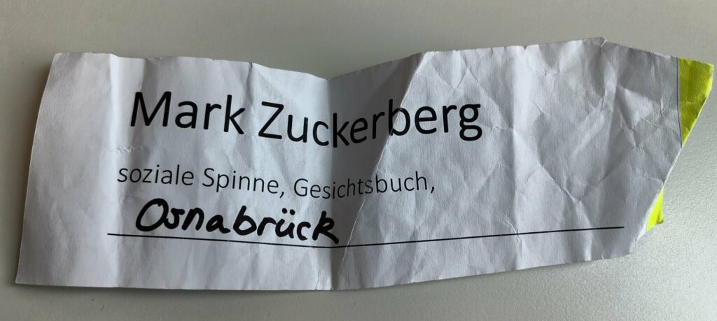 Ein Zettel, auf dem als Beginn eines Slogans für Mark Zuckerberg steht: "soziale Spinne", "Gesichtsbuch" und handschriftlich ergänzt "Osnabrück"